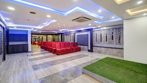 A modern conference room with a stage, red chairs, and a green carpet area. - Treebo Masterprice Inn - 15 Mins From Airport (Lucknow)