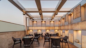 An outdoor patio area with round tables and wicker chairs, featuring a patterned wall and ceiling design. - Treebo Masterprice Inn - 15 Mins From Airport (Lucknow)