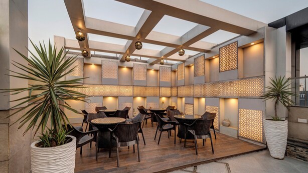 An outdoor patio area with round tables and chairs, decorative lighting, and large potted plants. - Treebo Masterprice Inn - 15 Mins From Airport (Lucknow)