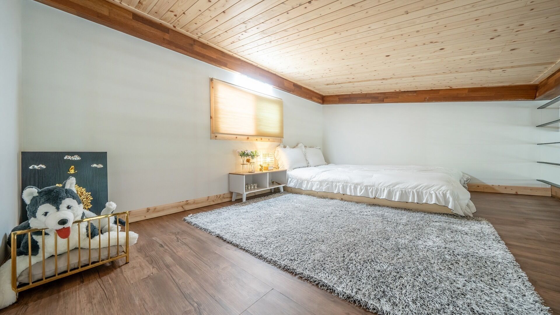 A bedroom with a wooden ceiling, a bed, a nightstand, a rug, and a wall-mounted shelf.