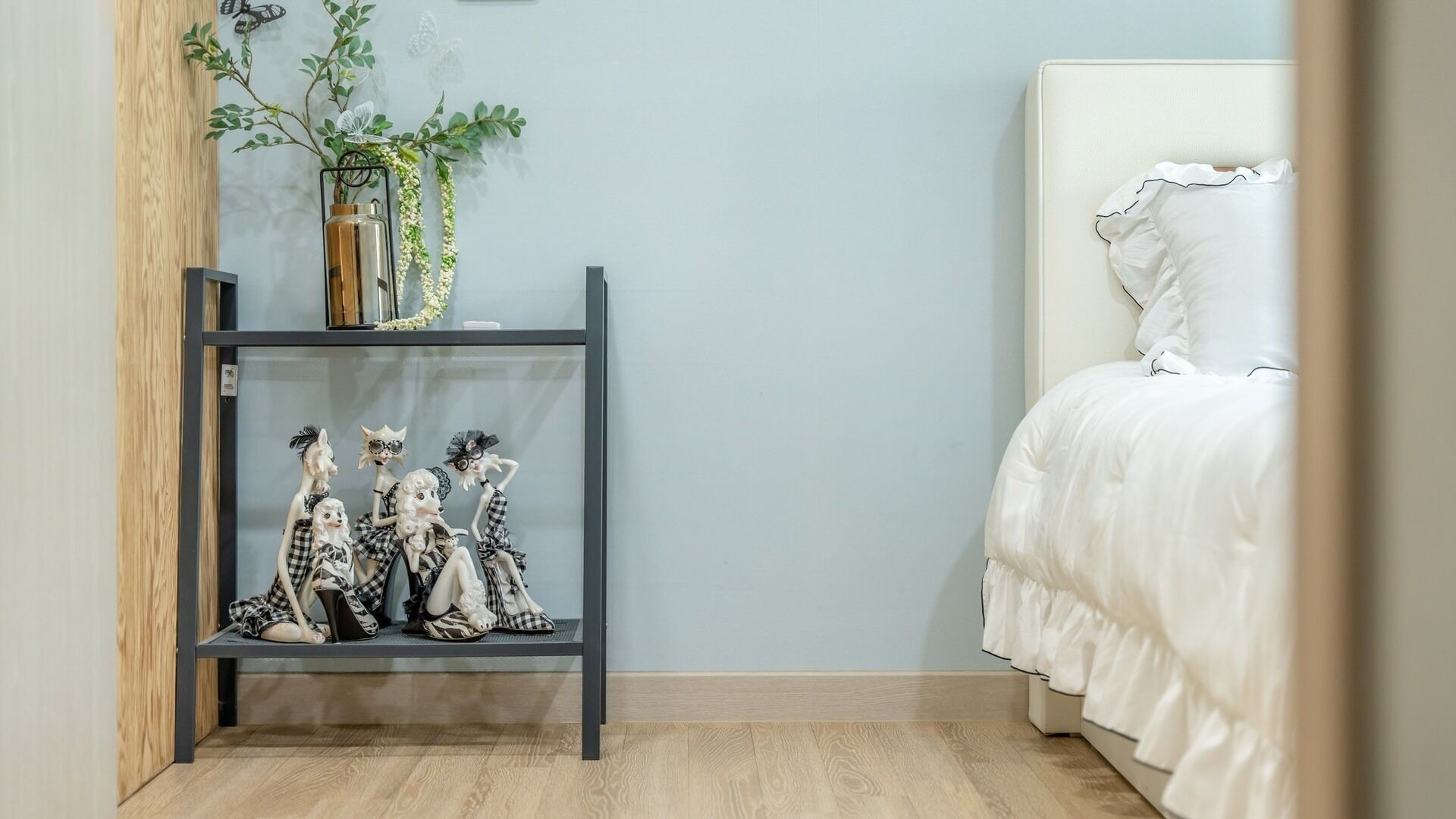 Une chambre à coucher avec un lit, une étagère ornée d’objets décoratifs et une plante.