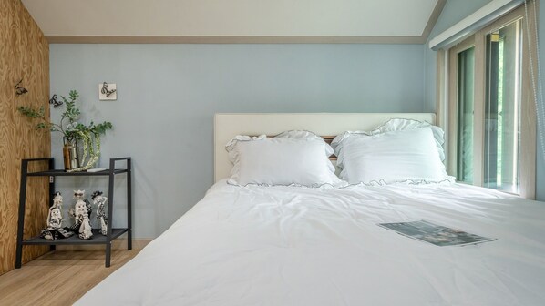 Un dormitorio con cama, mesita de noche, ventana y pared con planta.