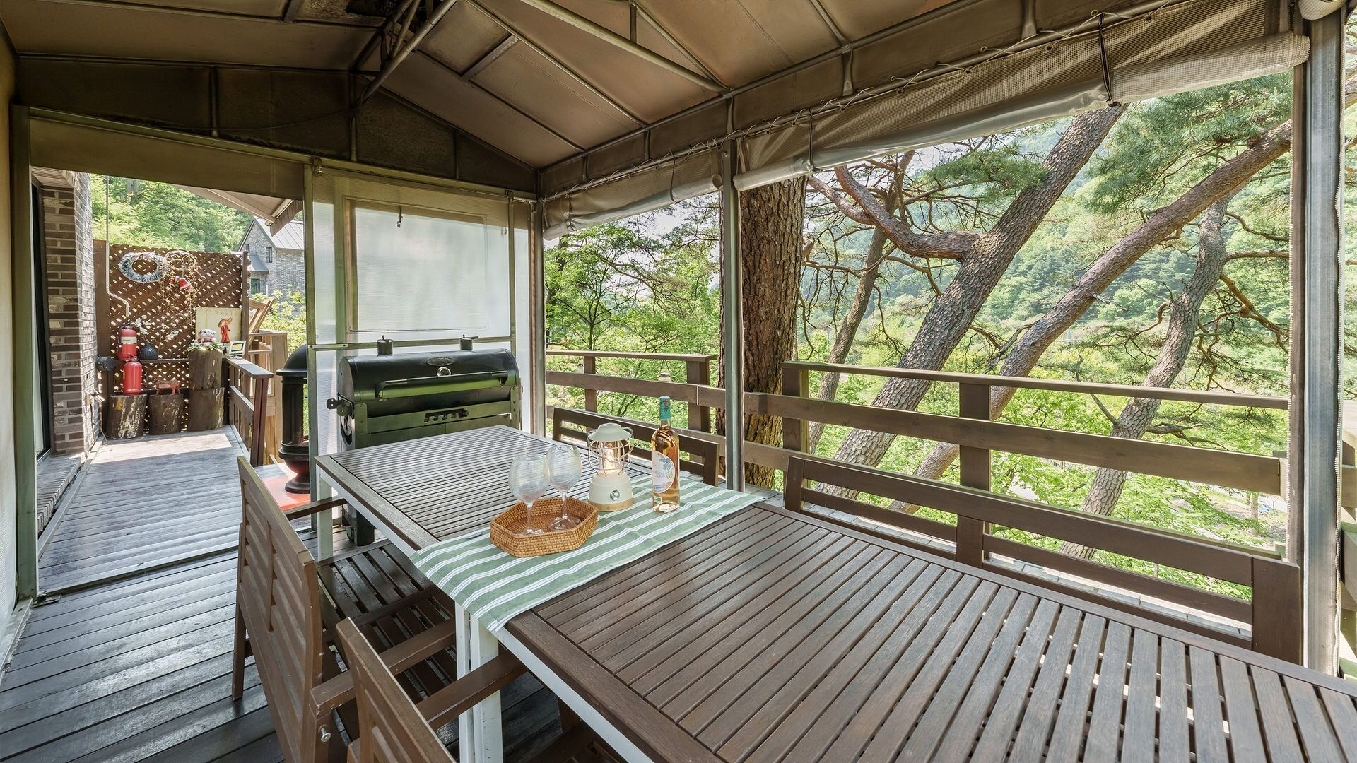 An outdoor wooden deck with a table, a grill, and a view of the forest.