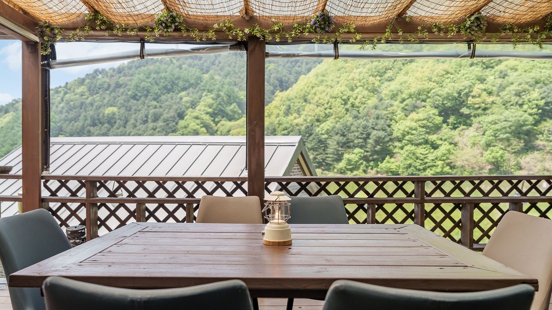 Ein Holztisch mit Stühlen und einer Laterne auf einem Balkon mit Blick auf einen bewaldeten Hügel.