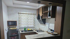 A compact kitchen with a built-in microwave, sink, and gas stove. There is a window with blinds, a ceiling light, and wooden cabinets. - Bimsy's Place  (Abuja)