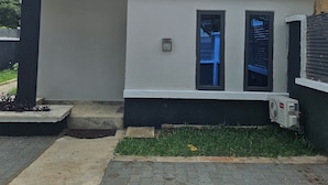 A modern building with a white facade, two windows with shutters, and a small air conditioning unit on the ground. - Bimsy's Place  (Abuja)