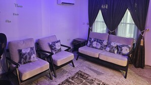 A living room with a sofa, two armchairs, a small table, and a rug. - Bimsy's Place  (Abuja)