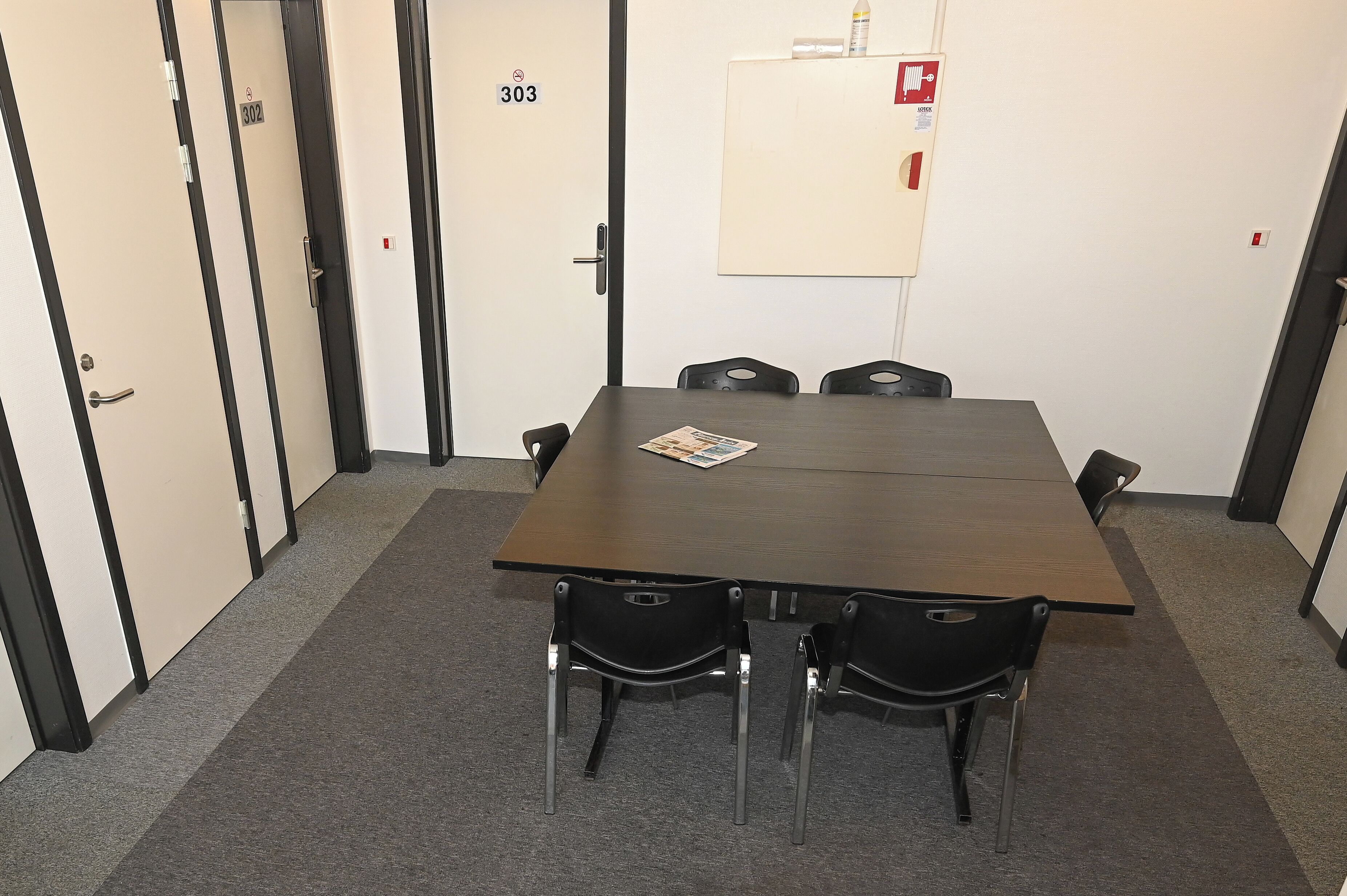 Une salle de conférence avec une longue table et quatre chaises. On y trouve des portes portant les numéros 302 et 303.