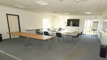 A conference room with a long table, multiple chairs, a whiteboard, and a projector screen.