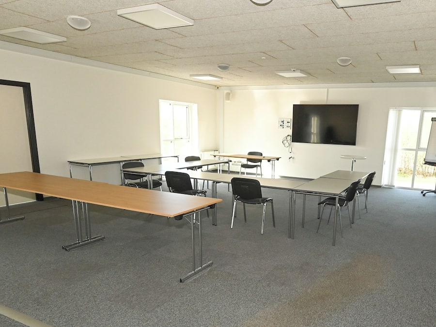 A conference room with a long table, multiple chairs, a whiteboard, and a projector screen.