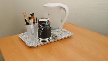 Una cafetera blanca sobre una bandeja, con un vaso de bolígrafos y una taza negra sobre una mesa de madera.