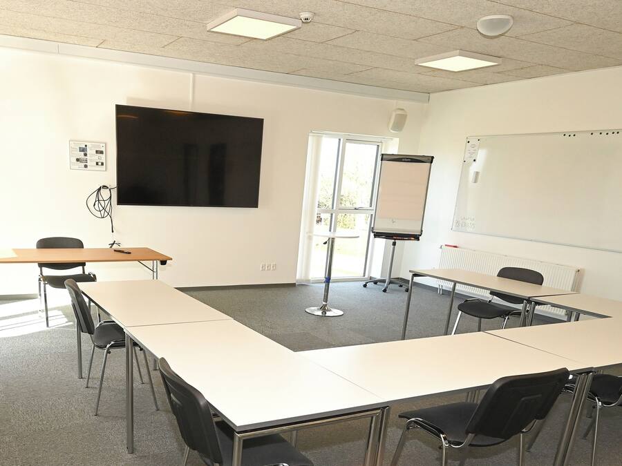 A conference room with a large table, chairs, a whiteboard, and a projector screen.