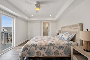 Un dormitorio con cama, ventilador de techo, mesita de noche y vistas al exterior.