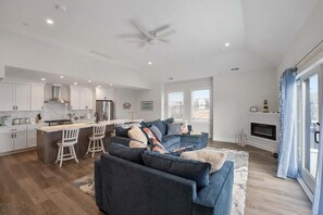 A modern kitchen with white cabinets, a central island with bar stools, a dark blue sofa, and a fireplace. - Oceanview Condo w/ a Rooftop Deck, Pool & Hot Tub! (Wildwood)