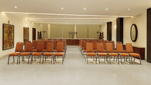 A conference room with rows of orange chairs, a stage with audio equipment, and a large mirror on the wall. - Oraka by My Downtown Aura Hotel (Udaipur)