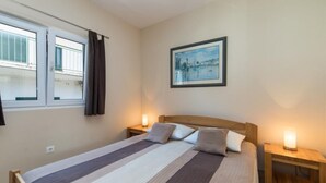 A bedroom with a bed, two bedside tables, a window with curtains, and a framed picture on the wall. - Apartments Nmn Drvenik (Gradac)