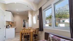 A compact living space with a kitchenette, a dining area, and a sofa with a floral cushion. - Apartments Nmn Drvenik (Gradac)