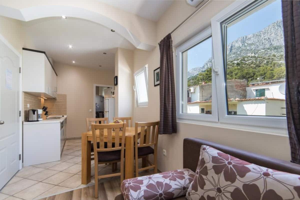 A compact living space with a kitchenette, a dining area, and a sofa with a floral cushion.