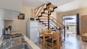 A compact kitchen with a built-in microwave, a stove, and a sink. A wooden dining table with chairs is positioned near a staircase leading to a balcony. - Apartments Nmn Drvenik (Gradac)