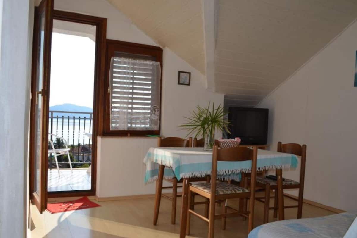 Una habitación pequeña y acogedora con balcón, una mesa de comedor con sillas, un televisor y una cama.
