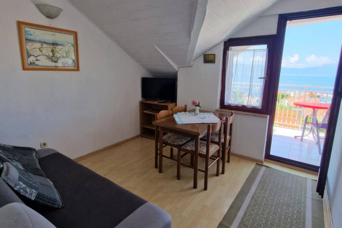 Una habitación acogedora con sofá, una mesa de comedor con sillas, televisor y un balcón con mesa y sillas rojas.