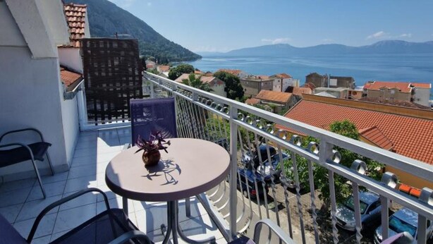 A balcony with a table and chairs, overlooking a coastal town with red-roofed buildings and a view of the sea and mountains. - Lora Apartments Gradac (Gradac)