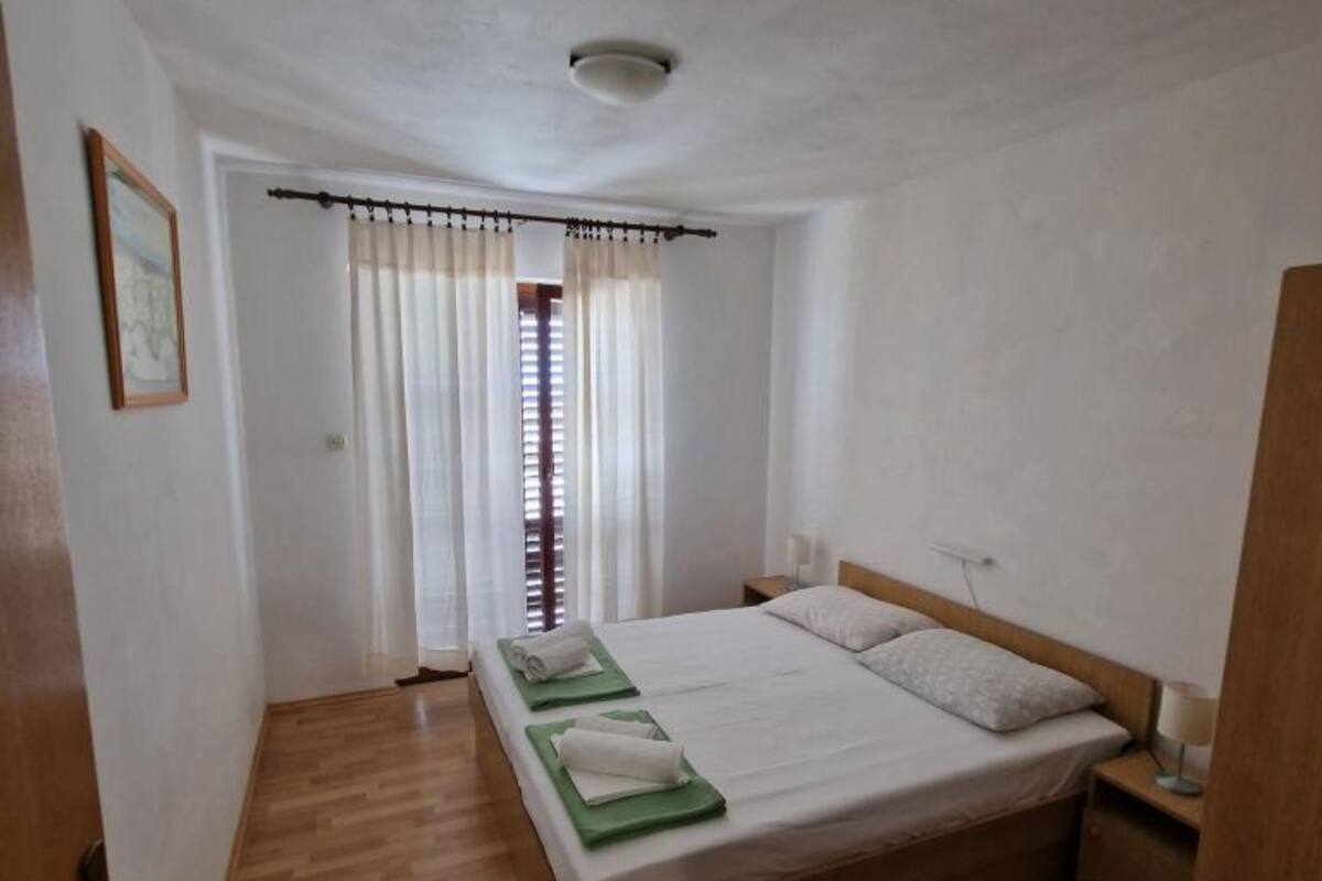 Una habitación pequeña y limpia con una cama individual, una mesita de noche y una ventana con cortinas.