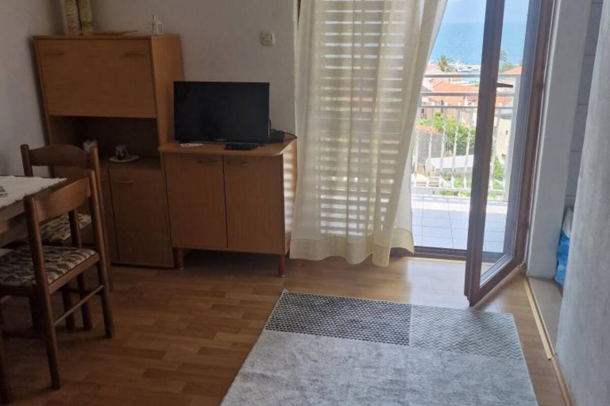 Una habitación pequeña con un escritorio de madera, un televisor y una ventana que da a vistas de edificios y al mar.