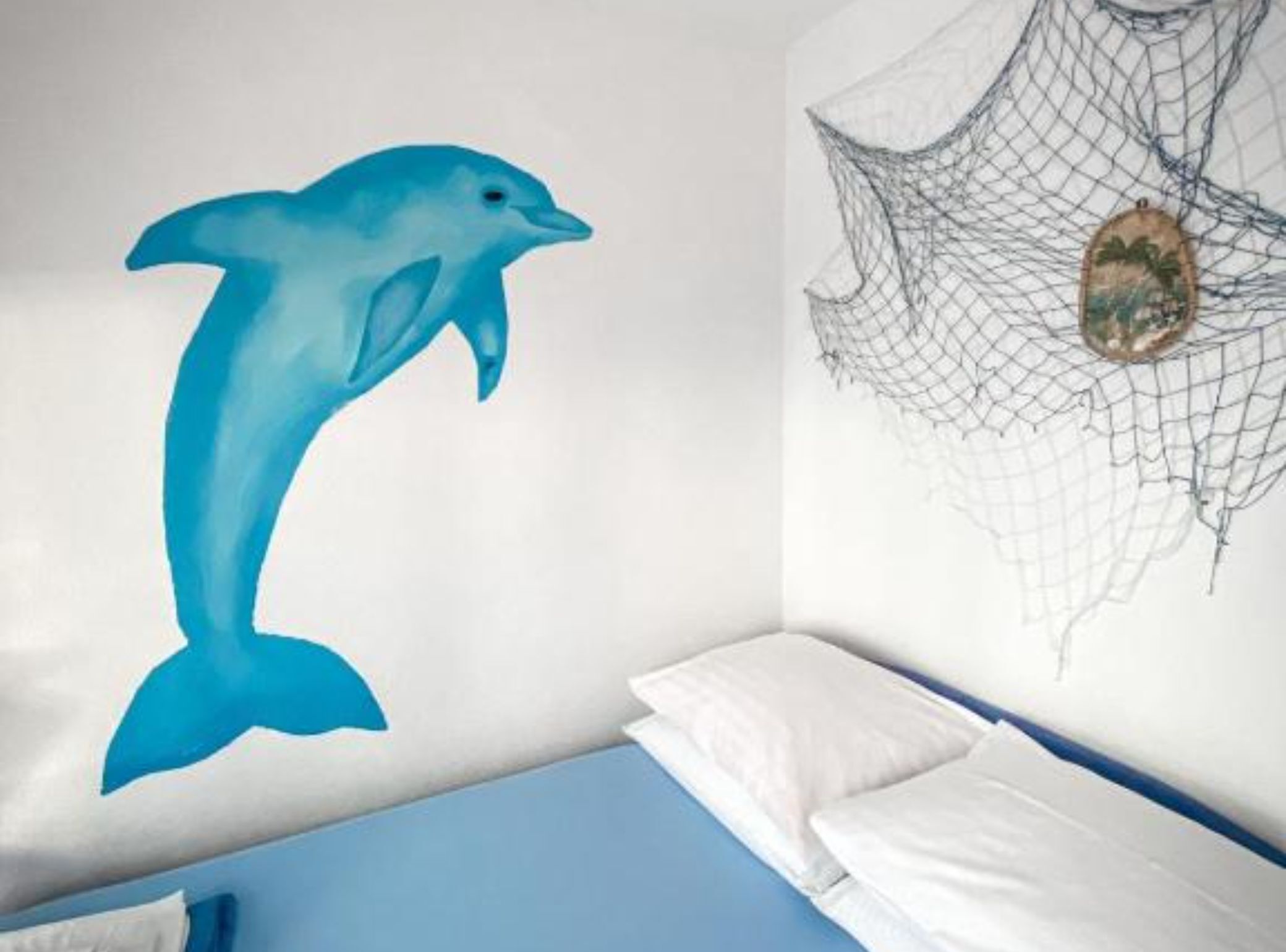 Une chambre avec un lit, un mur orné d’une fresque représentant un dauphin, et une décoration évoquant un filet.