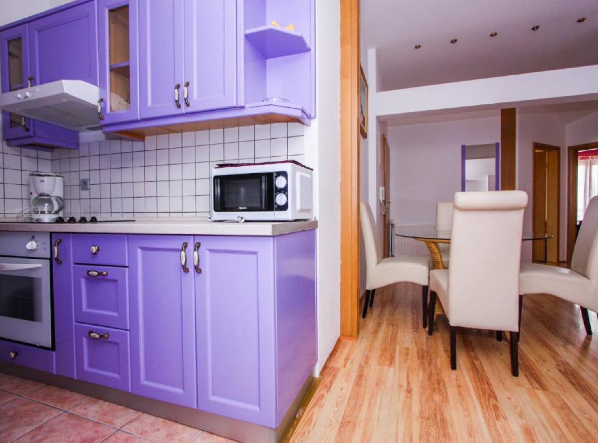 Una cocina con armarios morados, un microondas y una cafetera. Hay una zona de comedor con una mesa y sillas.