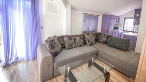 A living room with a grey sectional sofa, a glass coffee table, and purple curtains. - Peaceful Apartments With Style (Okrug)