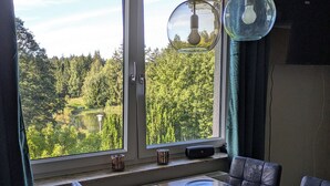 Un comedor con una mesa lista para cuatro, vista a un lago y un bosque a través de un ventanal grande, e iluminación colgante moderna.