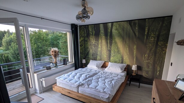 Un dormitorio moderno con una cama grande, vistas a un bosque por la ventana y un balcón.