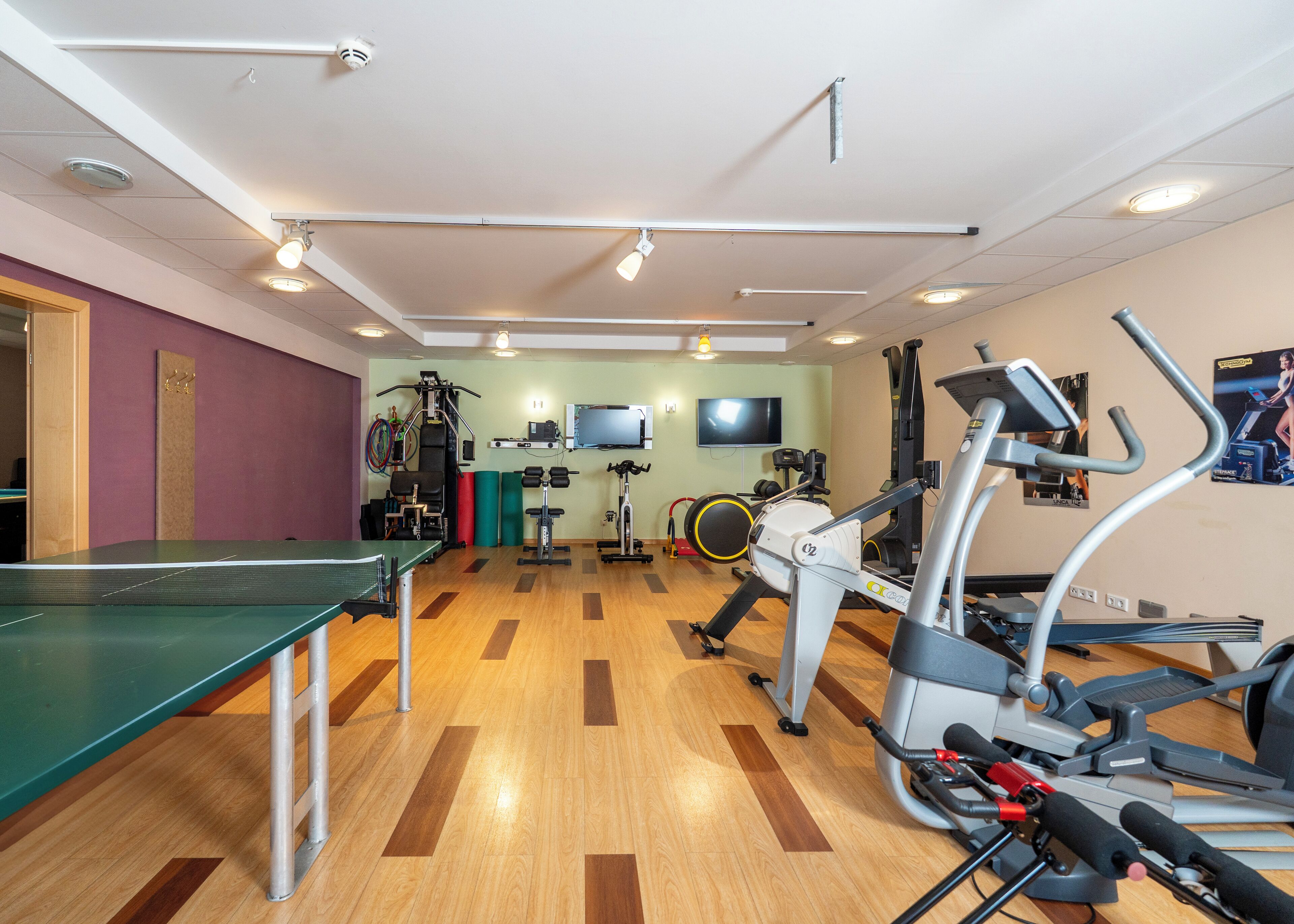 A gym with exercise equipment, a TV, and a ping pong table.