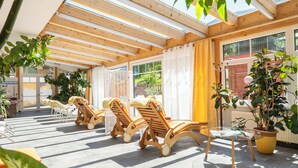 A sunlit patio with wooden lounge chairs, potted plants, and a glass table. - DAS Hubertus Apartments in Schladming (Schladming)