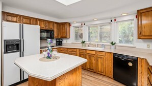 A modern kitchen with wooden cabinets, a white countertop, a black dishwasher, and a built-in oven.