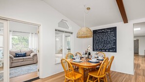 A dining area with a round wooden table, six wooden chairs, and a hanging woven light fixture. A chalkboard with writing is mounted on the wall.