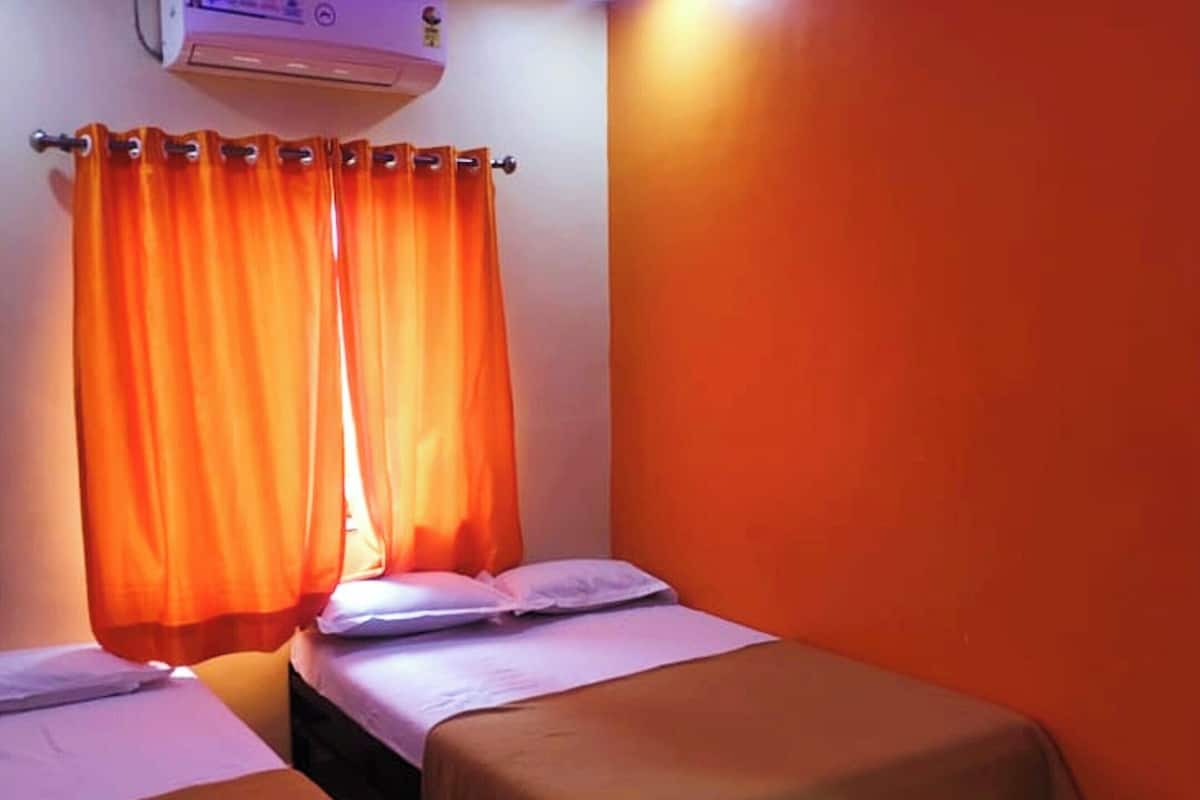 Una habitación con dos camas, cortinas naranjas, un aire acondicionado y un ventilador de techo.