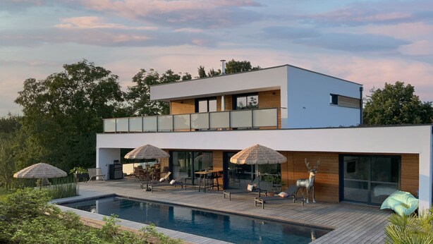 Une maison moderne à deux étages, dotée d’une piscine, d’un espace salon extérieur et d’une grande porte vitrée.