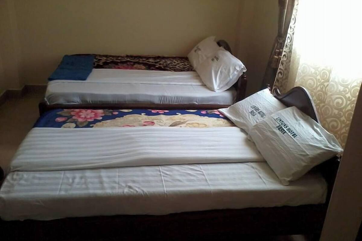 Quarto com três camas, cada uma com um edredom diferente. Há uma mala no lado direito da imagem.