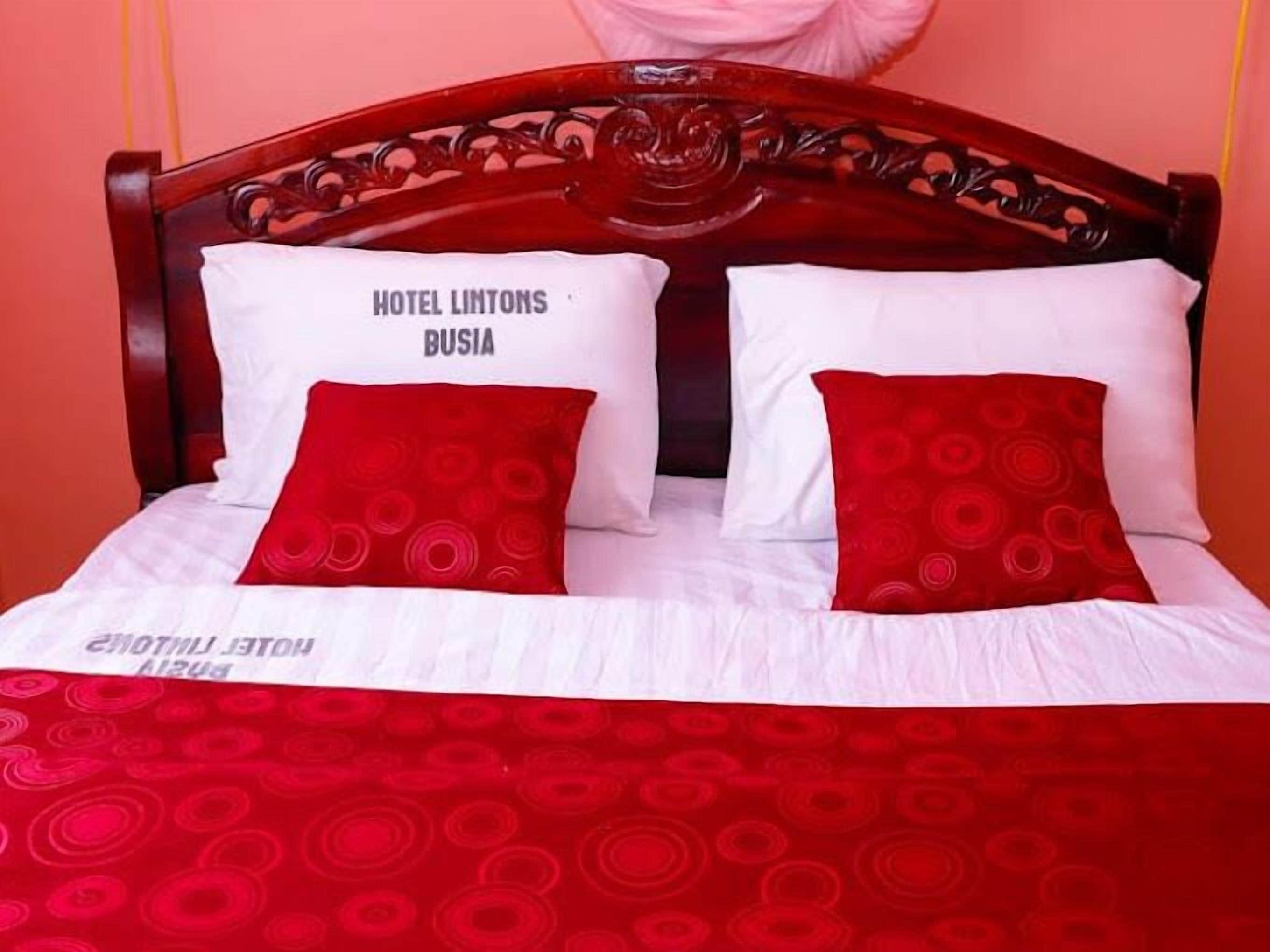 Un lit avec une tête de lit en bois, une literie blanche et des coussins rouges à motifs circulaires.