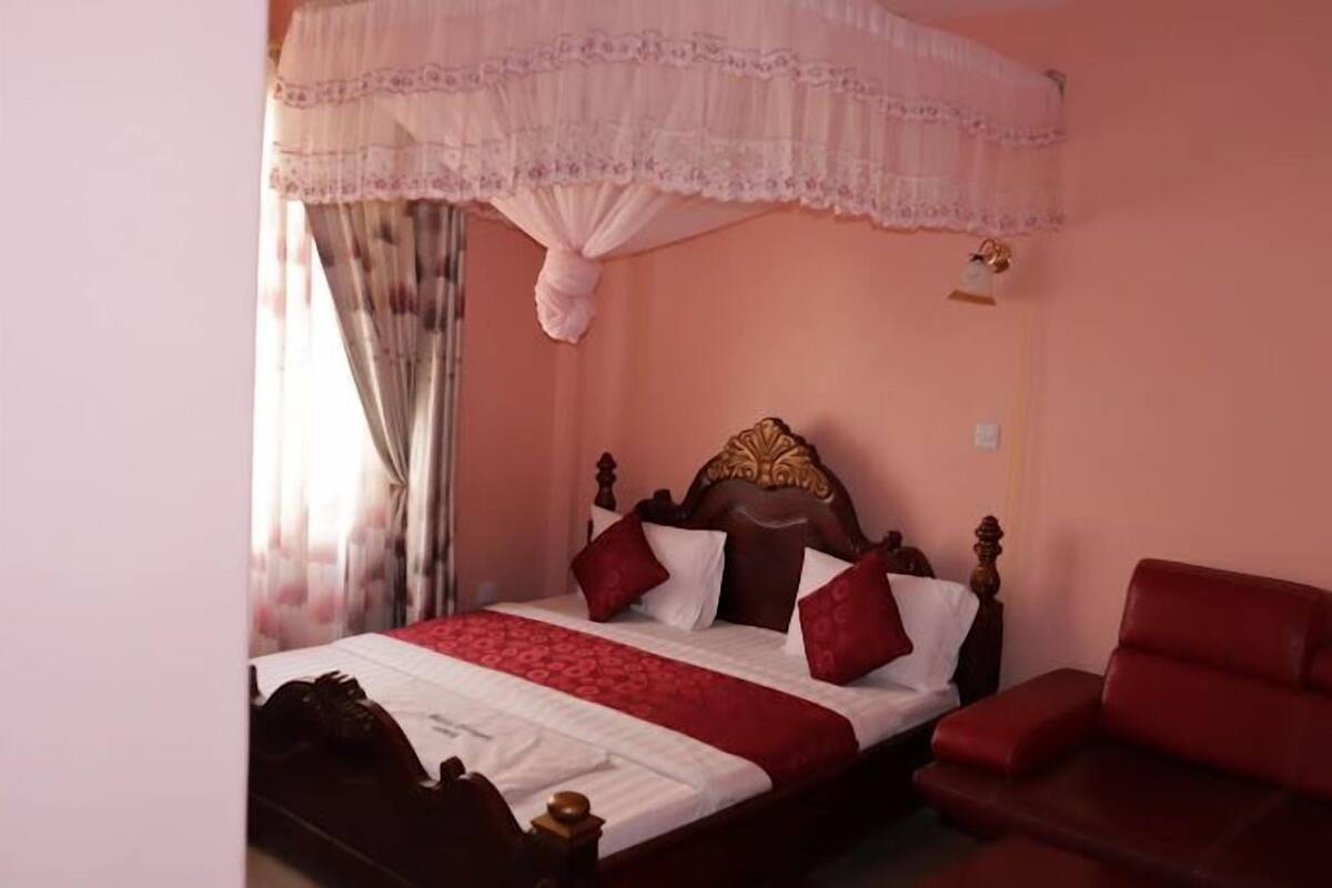 Quarto com cama de dossel, uma poltrona estofada vermelha e cabeceira de madeira.