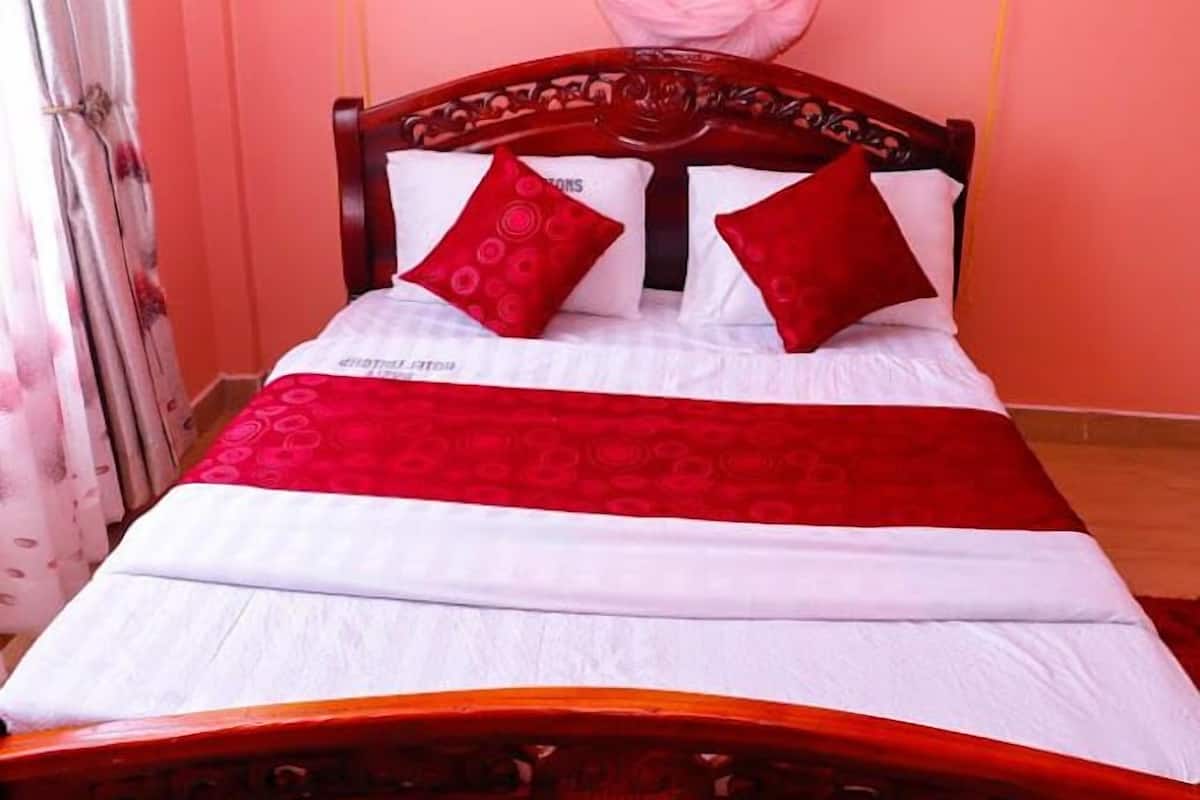 Cama com cabeceira de madeira, roupa de cama branca e almofadas vermelhas.