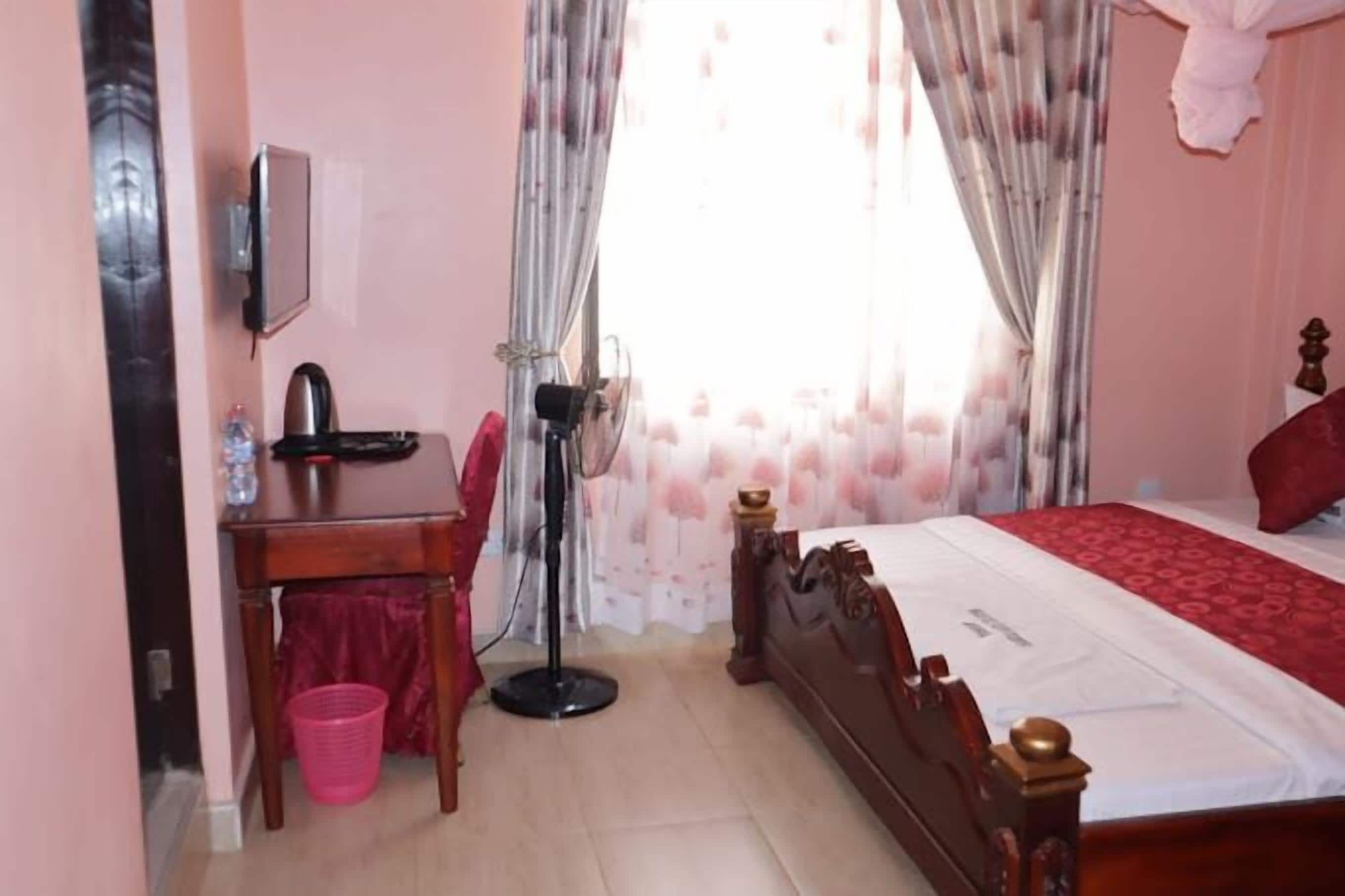 A bedroom with a wooden bed, a desk with a chair, a standing lamp, and a small trash bin.