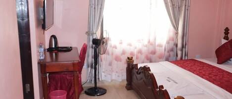 A bedroom with a wooden bed, a desk with a chair, a standing lamp, and a small trash bin.