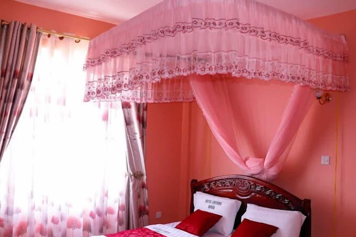 Quarto com cama de dossel, cortinas florais e parede vermelha.