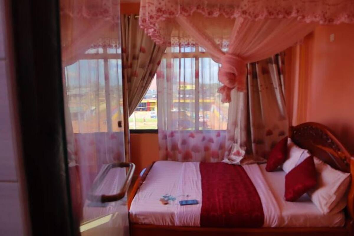 Quarto com cama, janela com cortinas e vista para o exterior.
