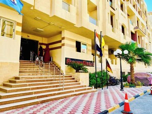 A hotel entrance with a staircase leading to the lobby, multiple flags, and a palm tree.