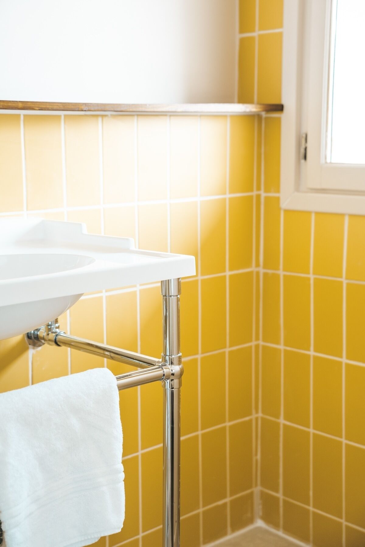 Un baño con lavamanos blanco, grifería cromada y paredes cubiertas de azulejos amarillos.