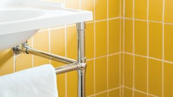 Un baño con lavamanos blanco, grifería cromada y paredes cubiertas de azulejos amarillos.